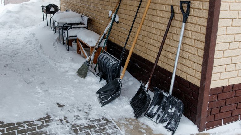 Different snow shovels leaning on a wall highlighting how heavy shovels tire you faster